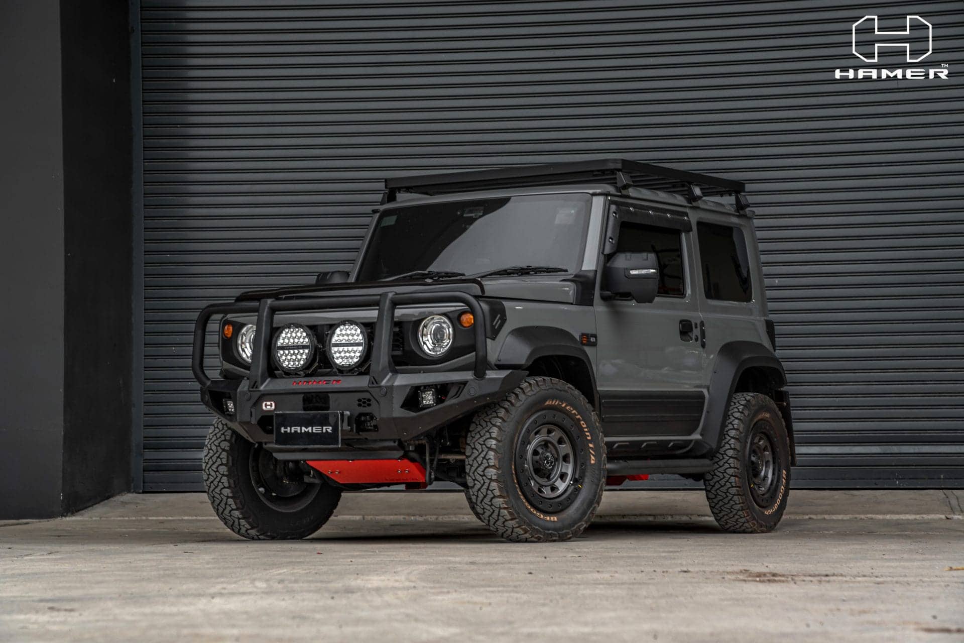Black off-road vehicle with bull bar and LED lights in front of a grey industrial door.
